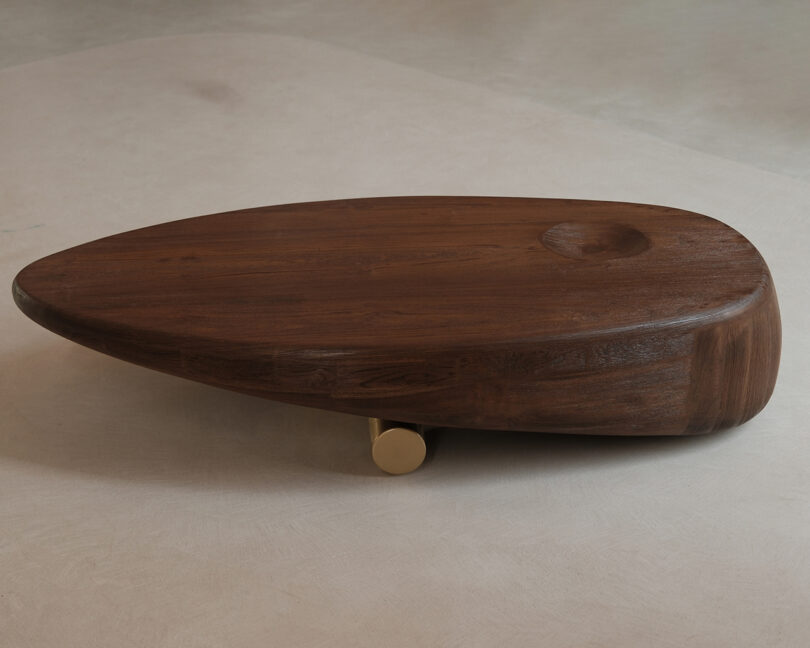 Low oval wooden coffee table with a single cylindrical brass leg and a smooth, carved top surface.