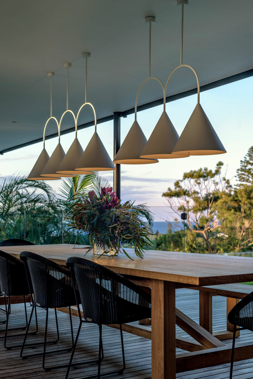 Outdoor dining area with black woven chairs, a wooden table, and glass railings overlooking green trees.