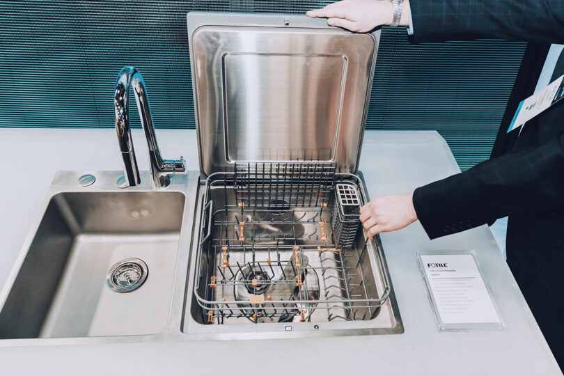A top-loading dishwasher integrated into a countertop next to a kitchen sink.