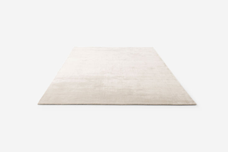 A white wool and bamboo rug placed under minimalist furniture.