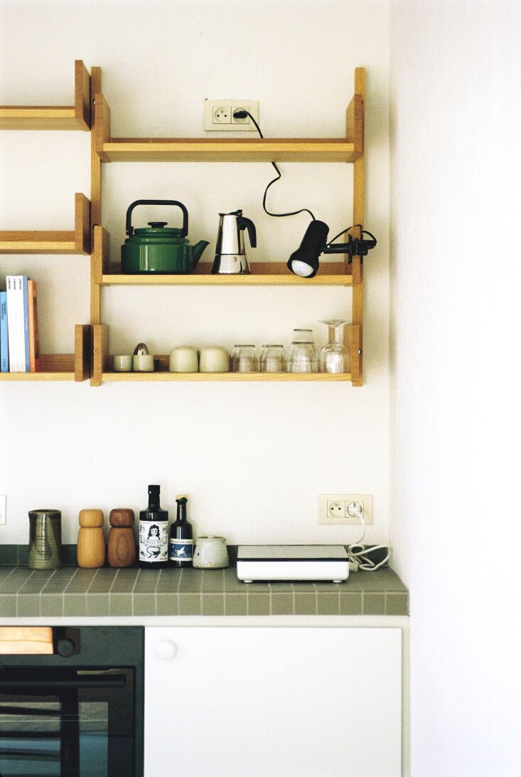 A minimalist kitchen corner with a portable induction cooktop, wooden shelving, and an Amu Kettle.