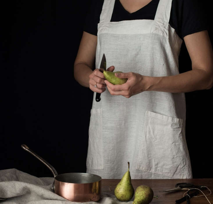 A person wearing a simple, high-quality linen pinafore apron in a home setting.