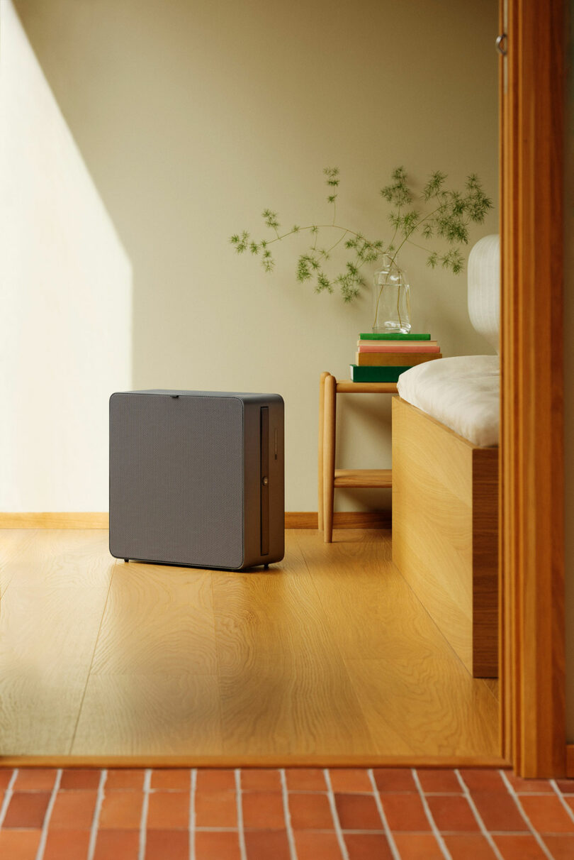 A gray Airthings Renew air purifier on a wooden floor in a minimalist room.