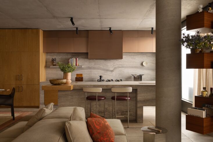 Modern kitchen with a travertine-clad island, birch plywood cabinets, and black contemporary bar stools.