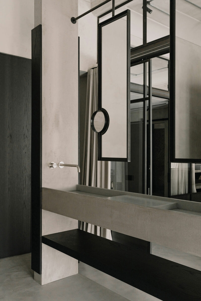 Modern bathroom sink made of concrete with a round mirror and dark wood accents.