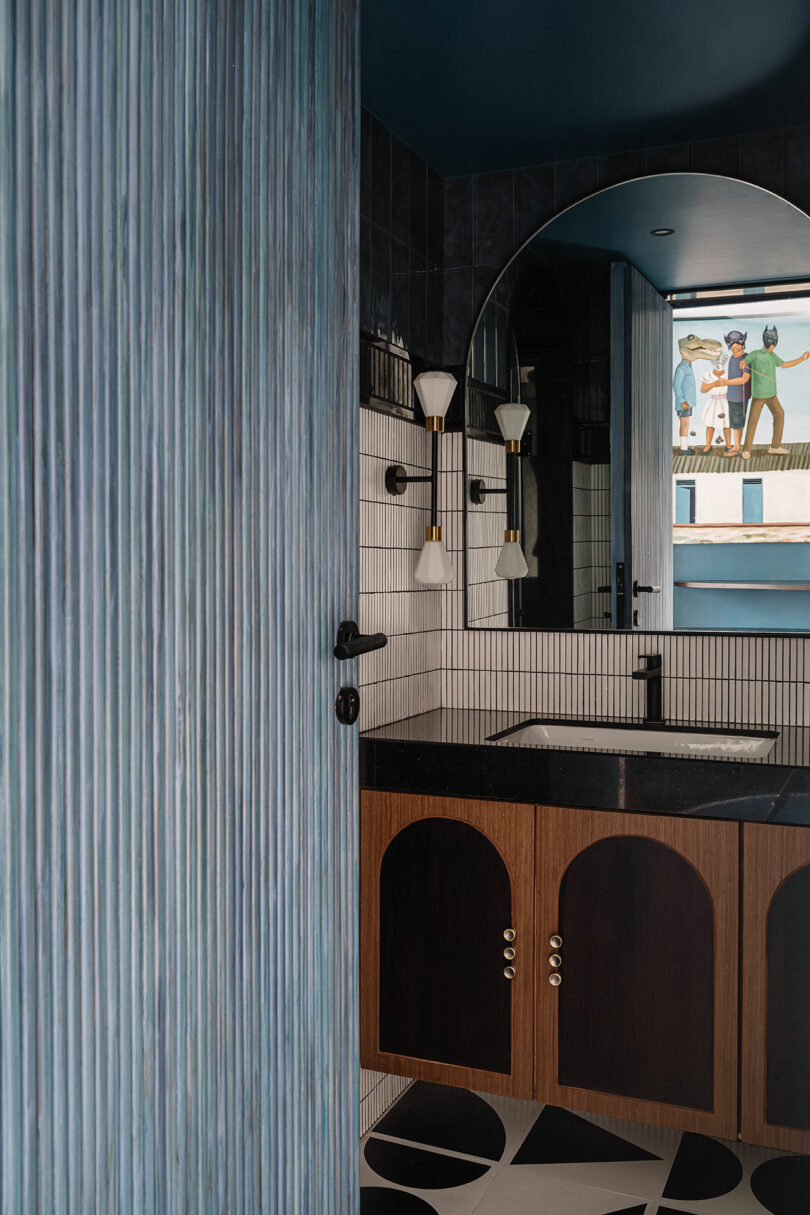 A bathroom featuring a blue ribbed wall, an arched mirror, and intricate geometric floor tiles.