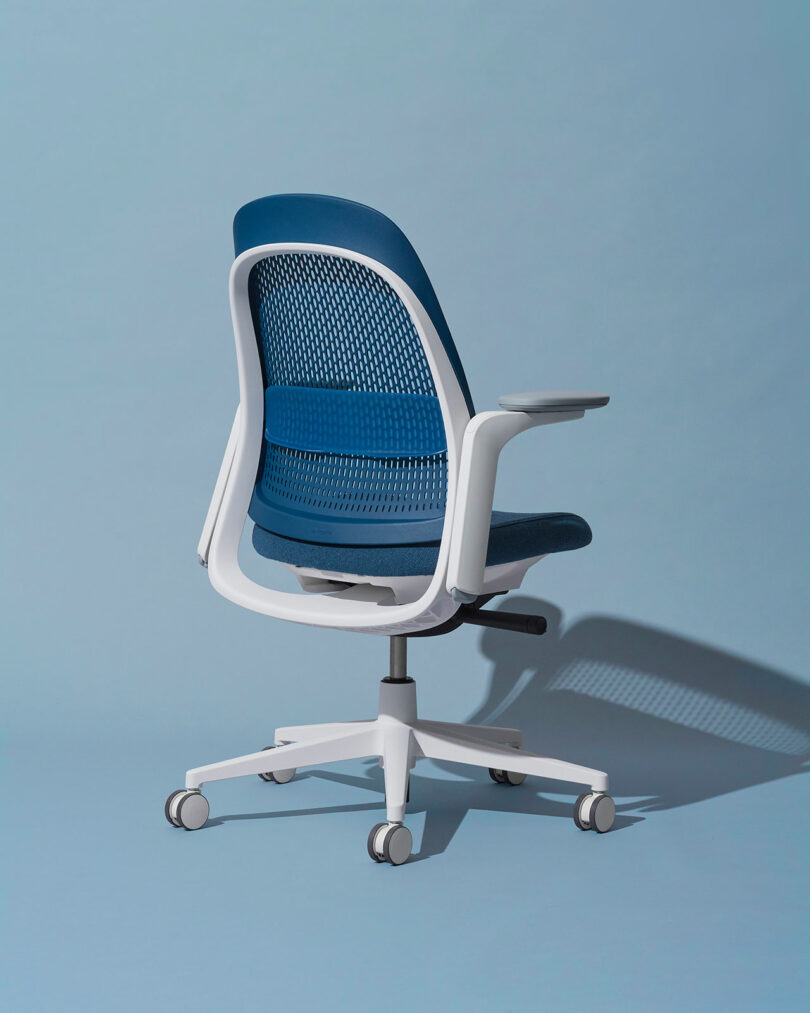 A rear-side view of a blue and white Haworth Breck chair, focusing on the mesh back and frame structure.