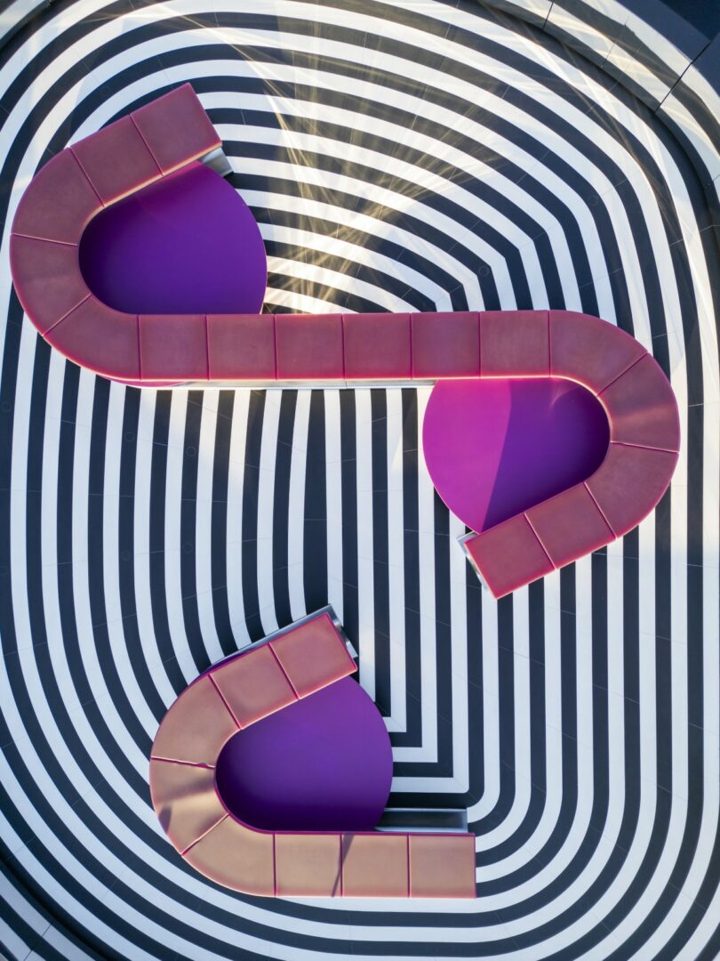 Top-down view of two curved purple benches placed on a concentric black and white oval patterned floor.