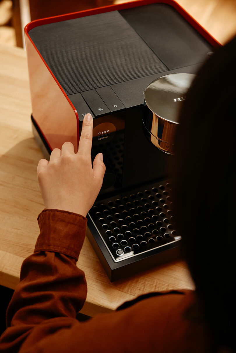 A close-up of a person's hand pressing a button on the Fellow espresso machine's control panel.