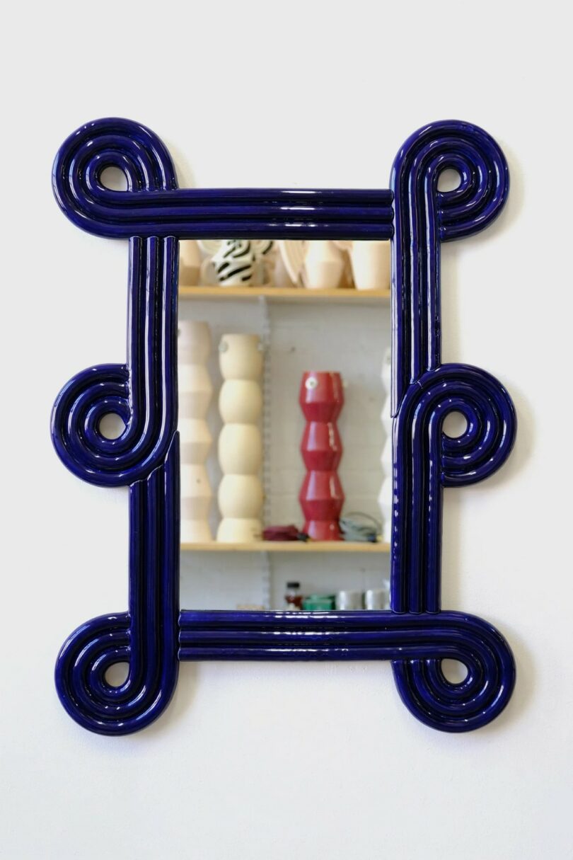 A glossy dark blue mirror frame featuring intricate ceramic coil designs.