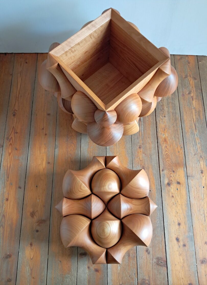 An open sculptural wooden box on a wooden floor, demonstrating its scale and internal volume.