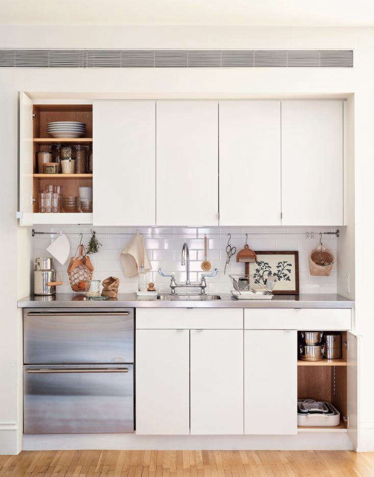Close-up of sleek metal tab pulls on light wood cabinetry in a compact kitchen.