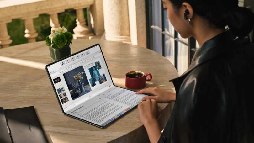 A person using a large foldable tablet at a round table with a coffee cup.