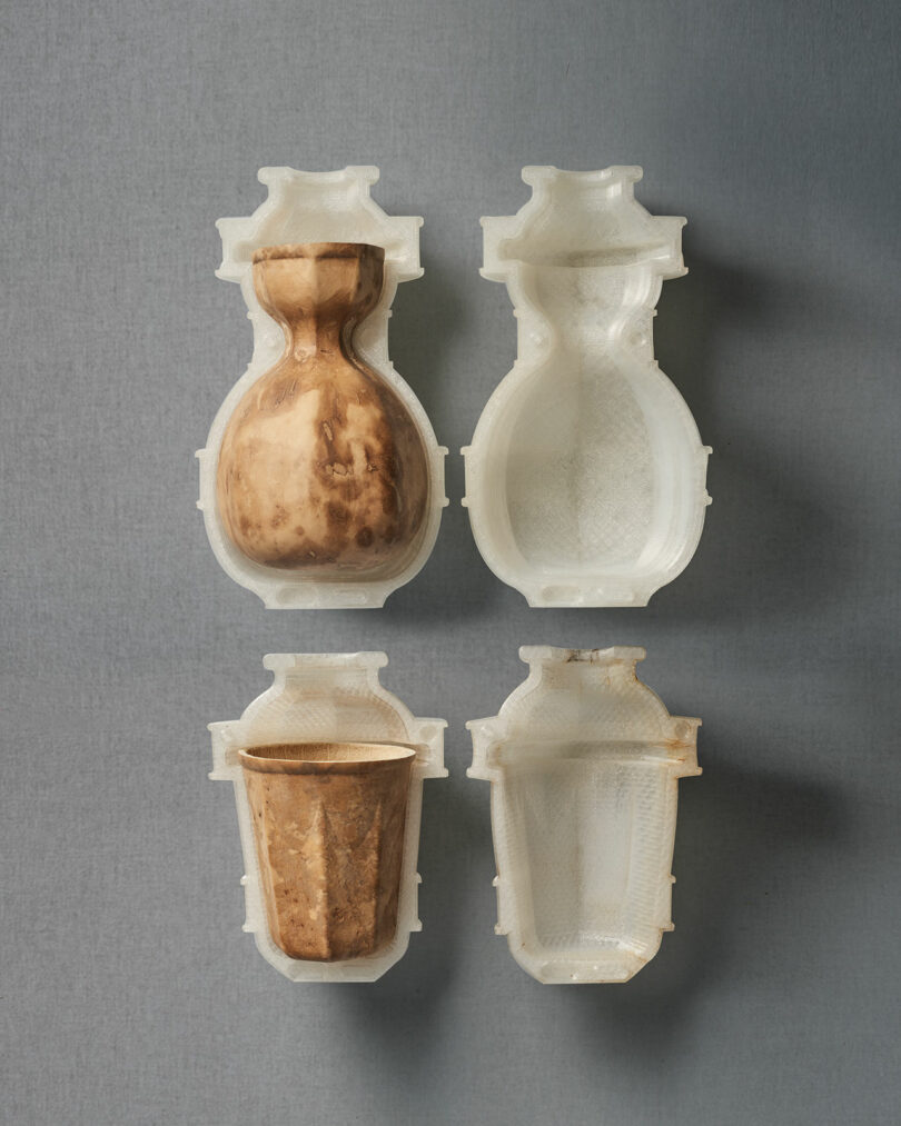 Two finished brown gourd vessels nestled inside the white 3D-printed molds used to shape them.