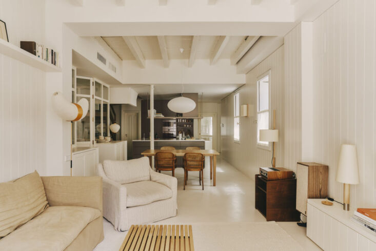 An expansive open-plan kitchen, dining, and living room with white walls and microcement flooring.