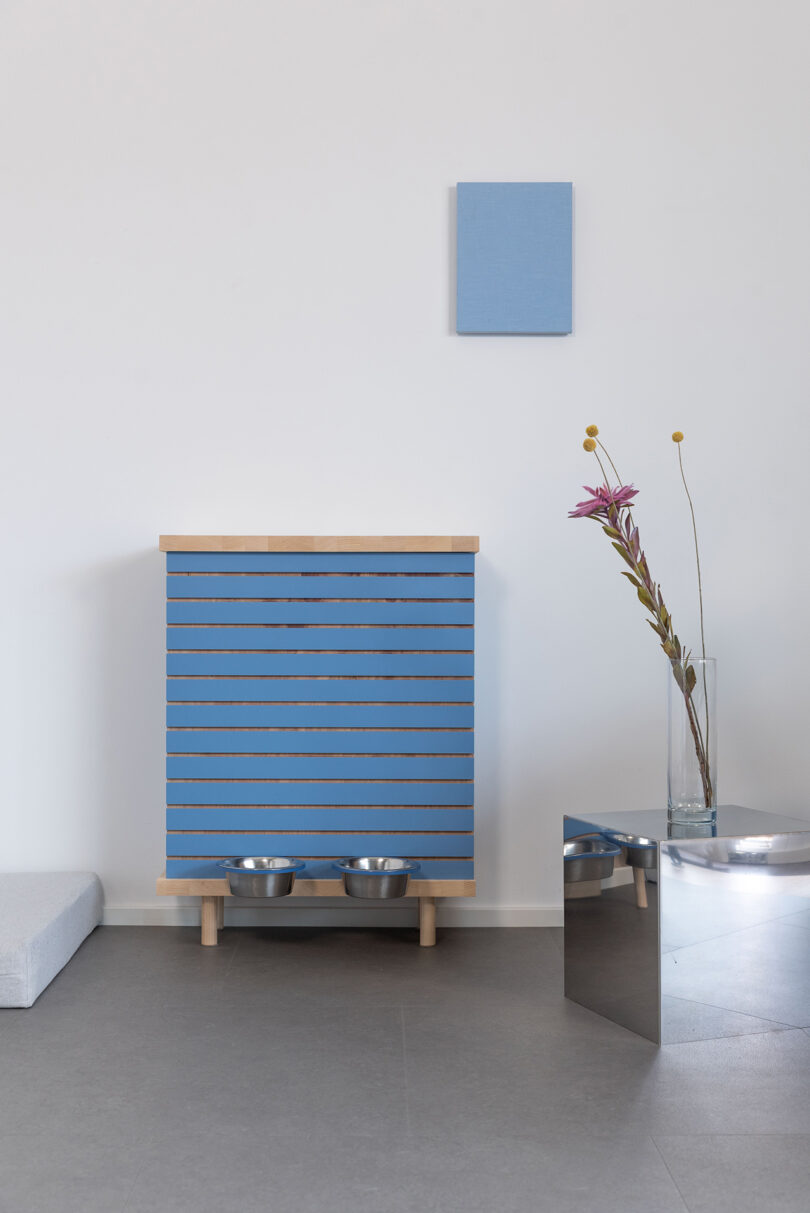 A minimalist living room featuring a blue-striped pet feeding cabinet and modern decor elements.