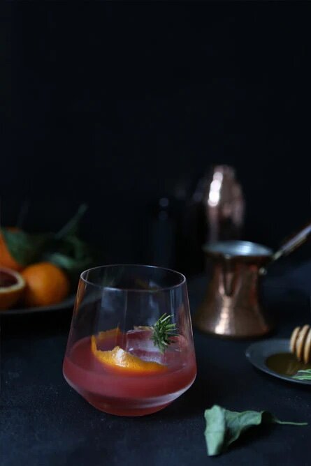 A blood orange cocktail served in a clear glass with a fresh rosemary sprig garnish.