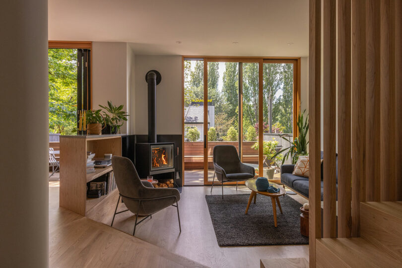 Modern living room with a wood-burning stove and floor-to-ceiling windows showing a forest deck.