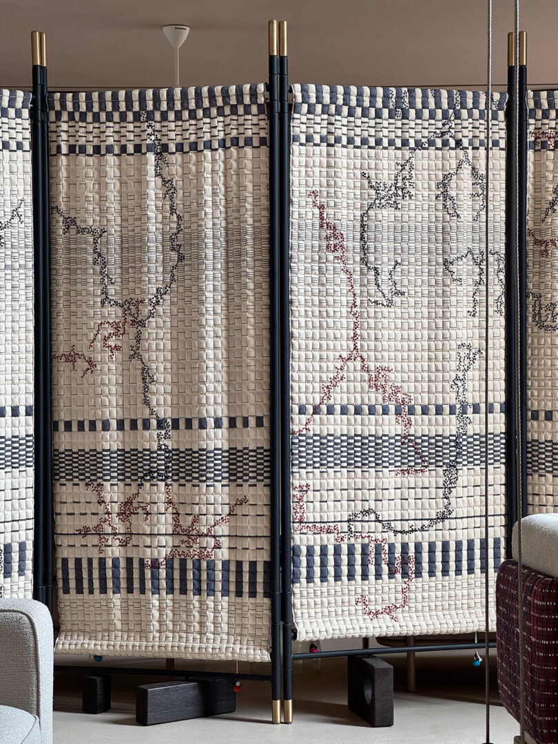 A checkerboard pattern room divider made of Sujani quilted fabric supported by a minimalist black frame.