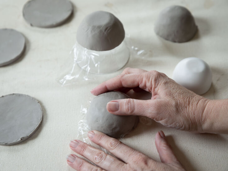 Clay being shaped over a jar covered in plastic wrap to create a vessel shape.