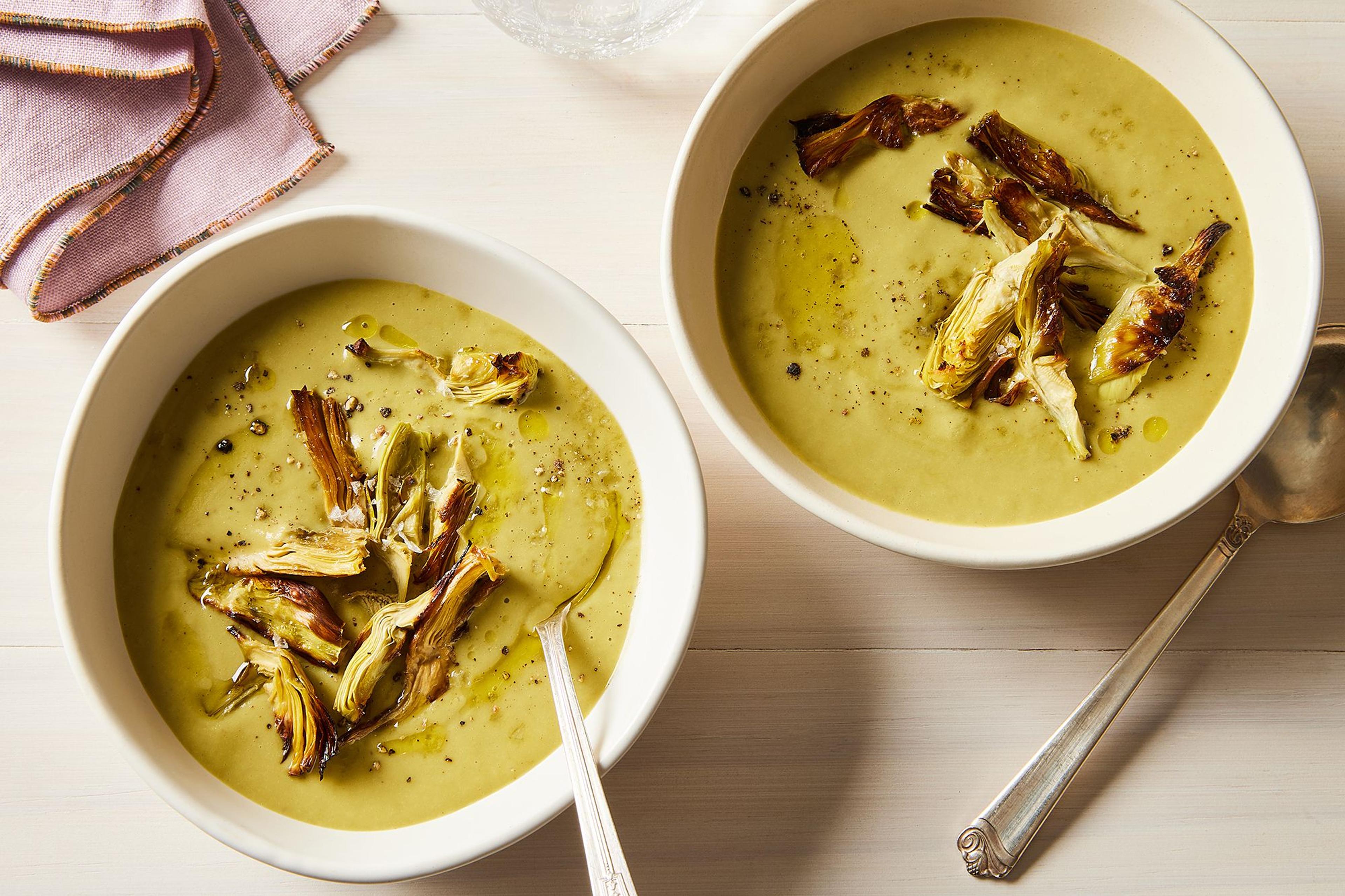 Two bowls of vibrant, smooth vegetable soup with cream garnish