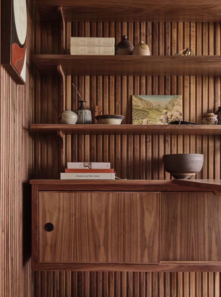 Close-up of custom walnut shelves holding various vintage ceramic pots and a small landscape painting.