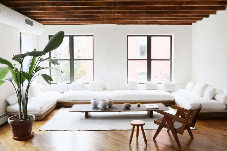 A modern white built-in sofa integrated into a minimalist NYC living room with wooden accents.