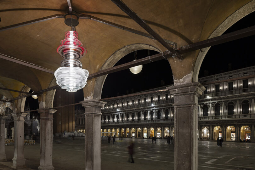 A spiral light fixture hanging under an arched stone walkway at night in Venice.