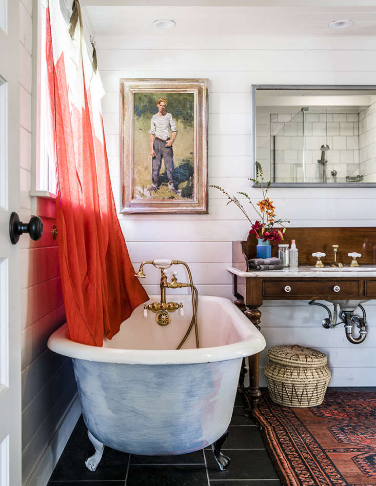 A vintage 1920s clawfoot tub in a white bathroom with signal flags used as window curtains.