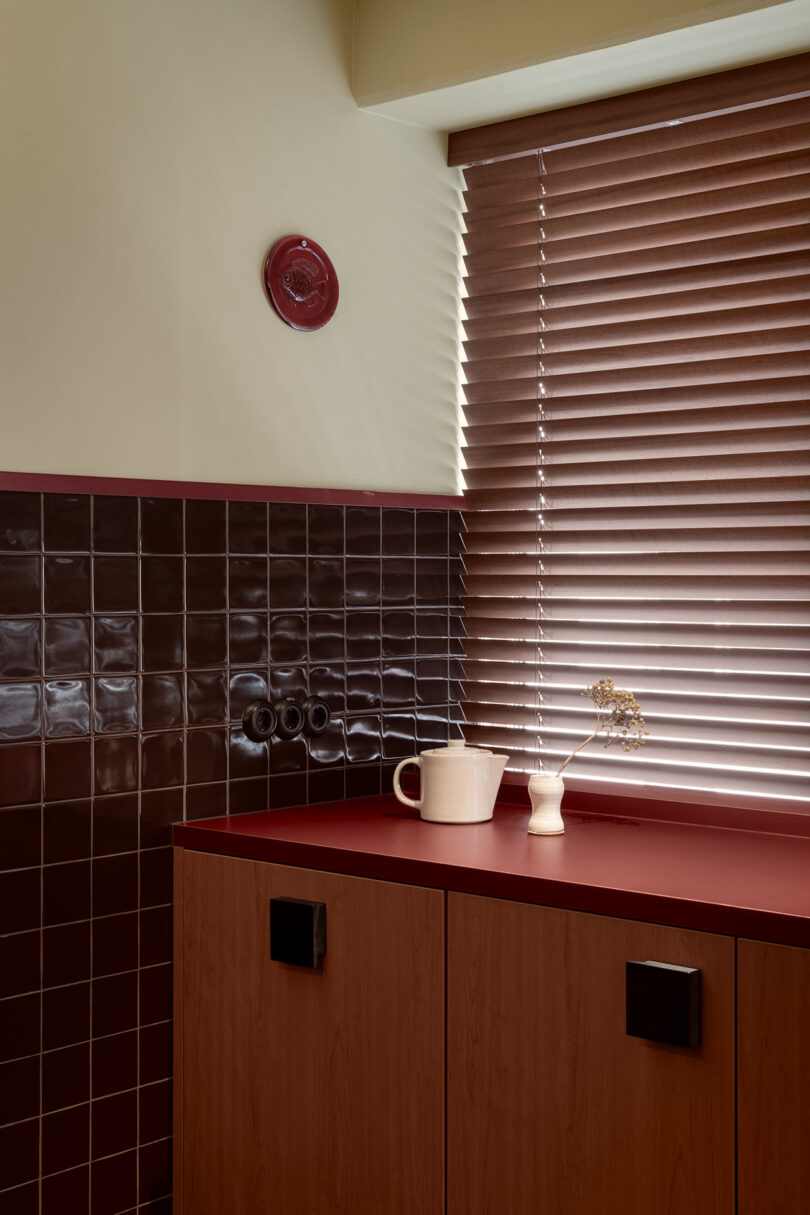 A kitchen corner with dark red tiled backsplash, red countertop, and wooden cabinets.