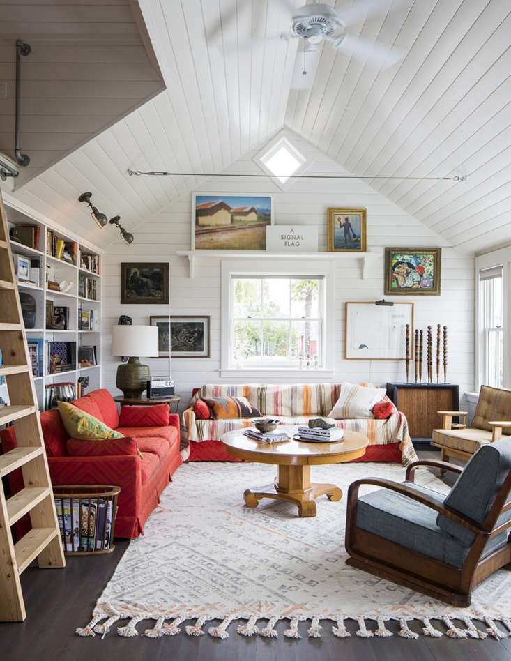 A cozy living room featuring a library wall, white cedar paneling, and nautical antiques.