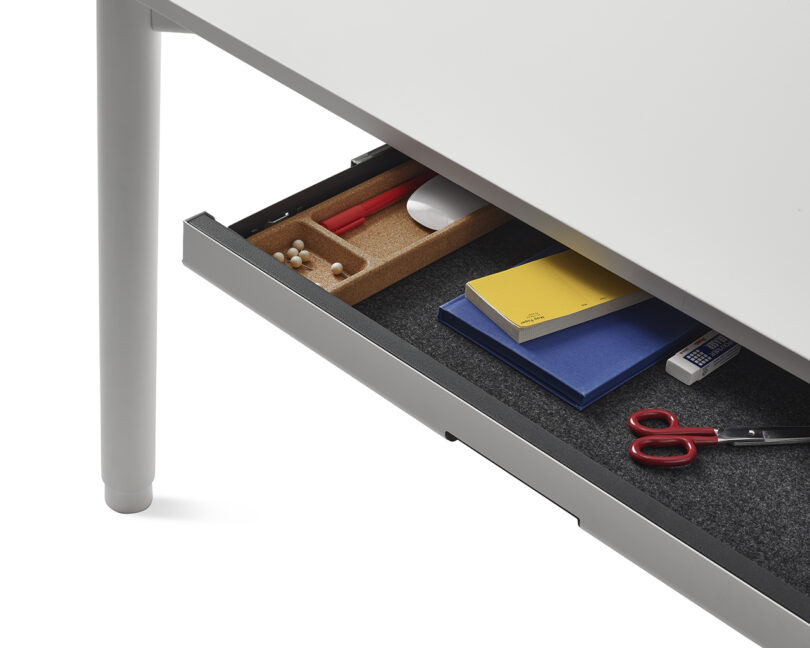 An open under-desk drawer showing neatly organized stationery, pencils, and notebooks.