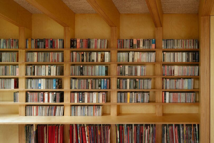 Wooden shelves filled with organized CDs and vinyl records inside a room with a timber interior.