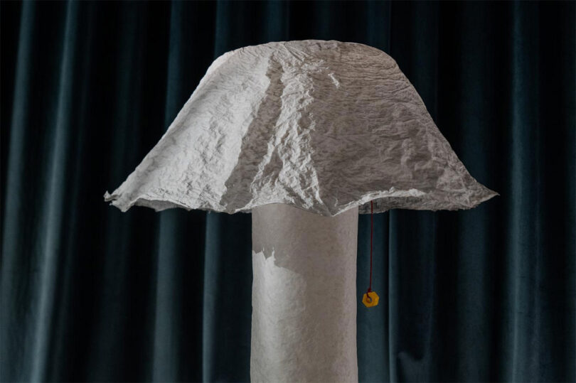 A floor lamp with a crumpled white paper-textured shade casting soft light against dark pleated curtains.