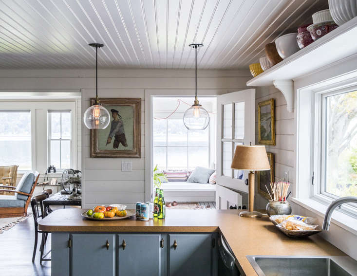 Gray-blue kitchen cabinets with brass hardware and white Formica countertops.