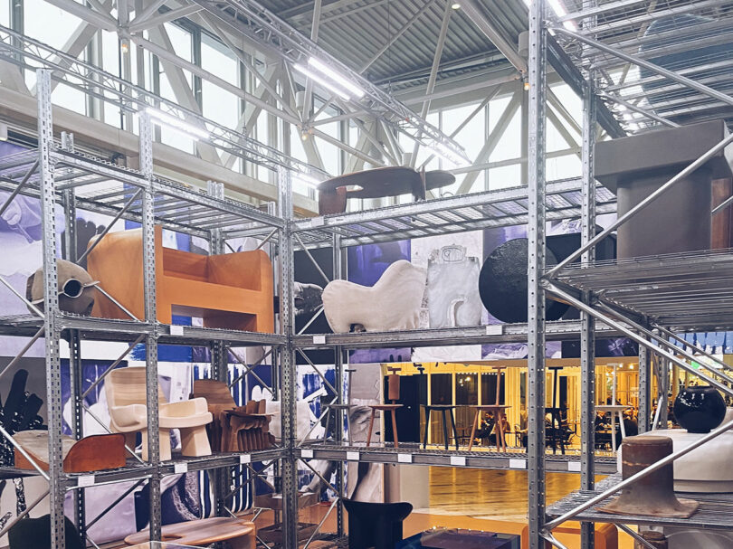 An industrial-style showroom with high ceilings and metal shelving displaying contemporary design pieces.