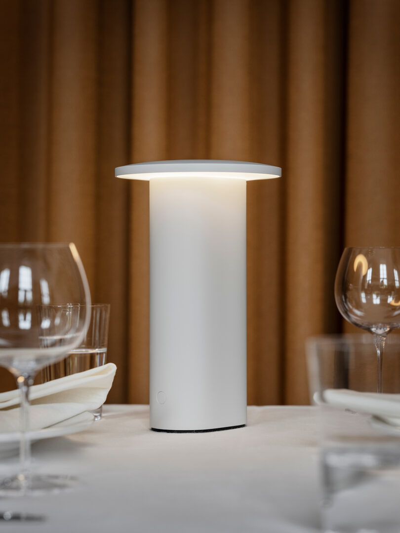 A glowing white Solae lamp on a set dining table with a warm background.