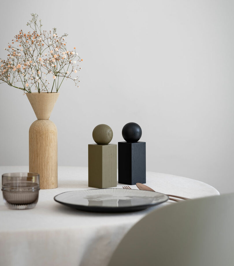 A minimalist and elegant table setting featuring a white tablecloth, a wooden vase, and two TWIST grinders.
