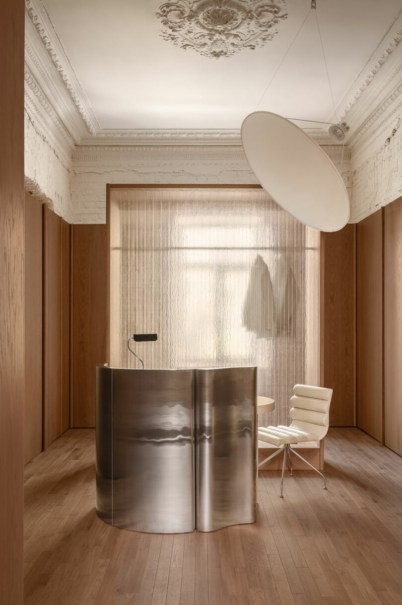 A curved metallic reception desk set against a backdrop of historic white wall moldings and sheer curtains.