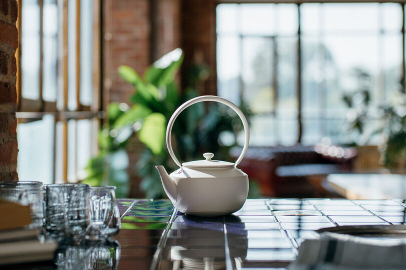 A white BALMUDA MoonKettle on a sunlit tiled counter featuring its distinctive loop handle.
