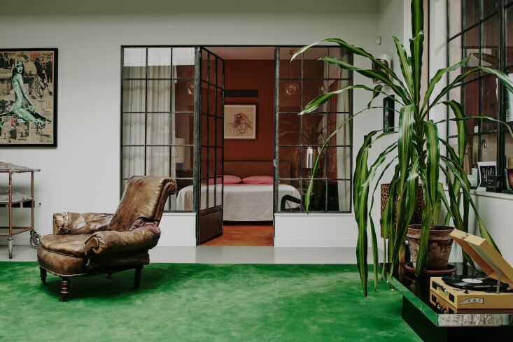 An interior space with a green carpet and large salvaged steel windows used as a room divider.