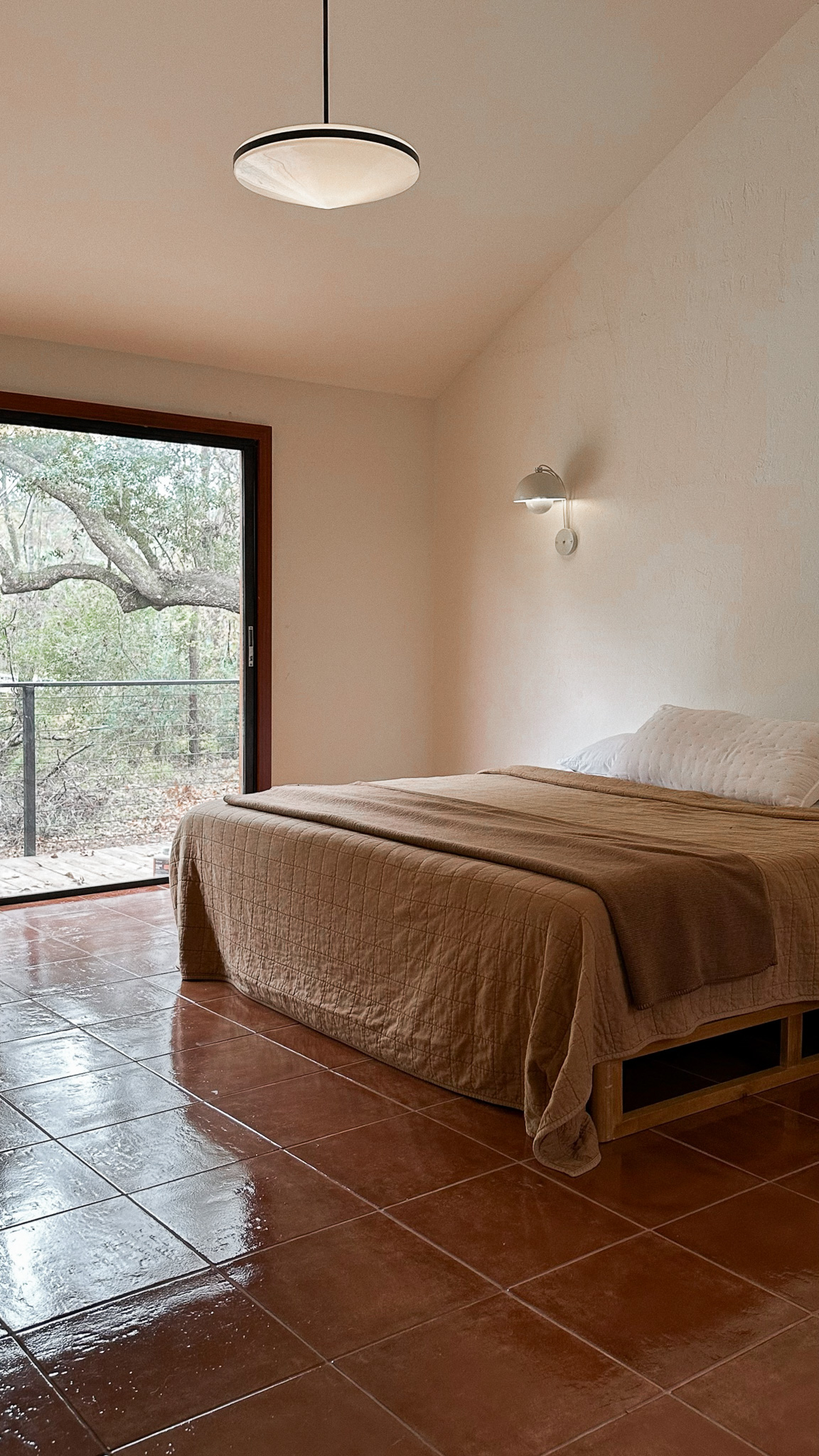 A primary bedroom with a 16-foot vaulted ceiling, white walls, and a large window looking out into the trees.