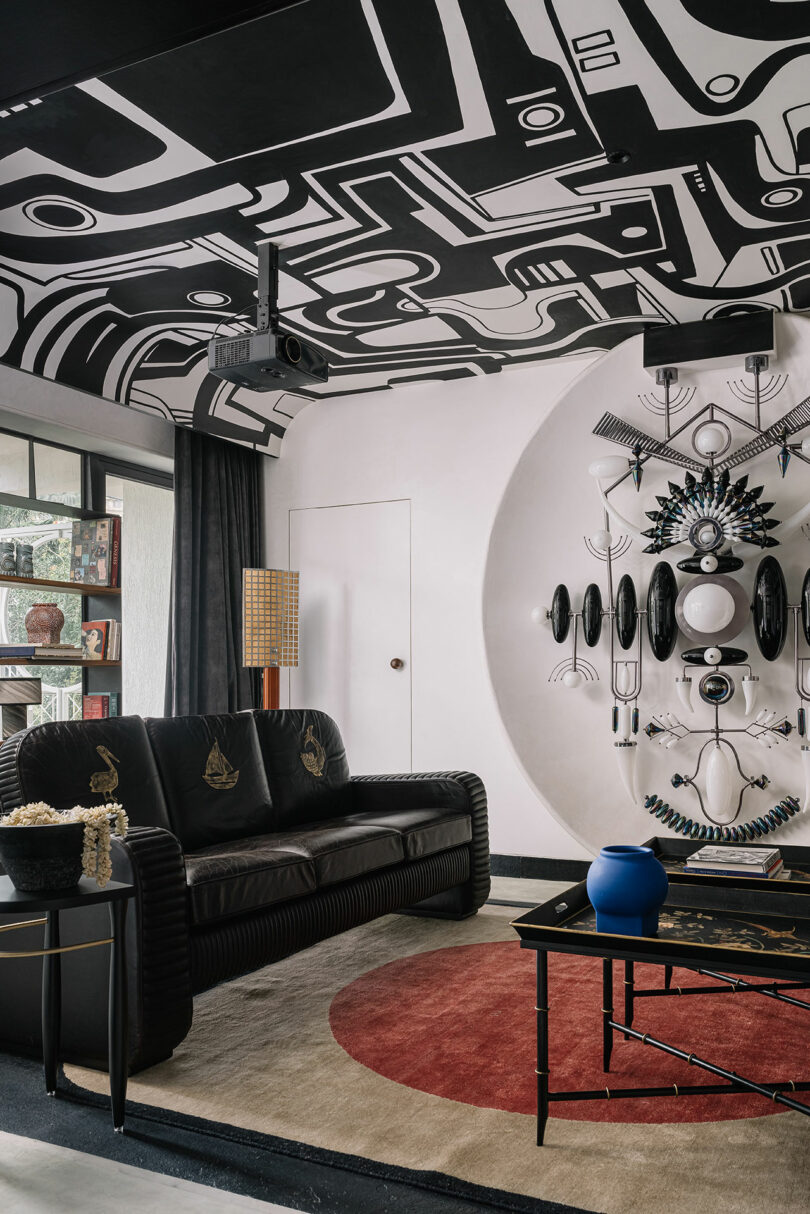 A room with a striking black-and-white geometric ceiling pattern, a black sofa, and a bold circular rug.