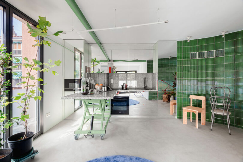 A modern kitchen with an adjustable-height table and green tile accents.