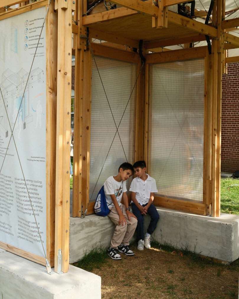 Two children sitting on a bench inside the wooden KlimaKover shelter.