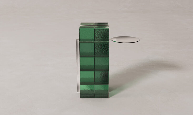 A green glass-block pedestal with a small white circular shelf protruding from the side.