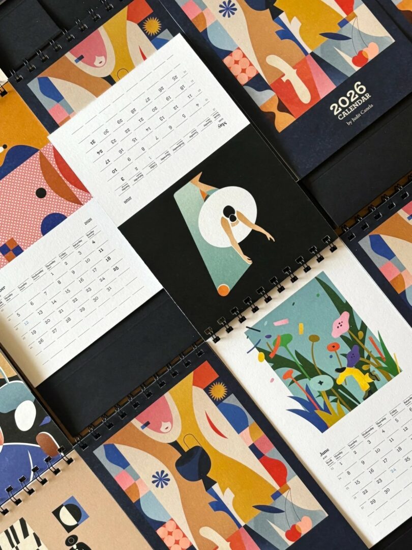 An open spiral-bound 2026 calendar with abstract colorful illustrations on the monthly pages.