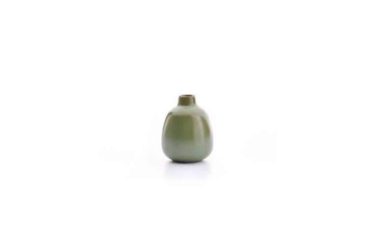 A small olive-toned Heath Ceramics bud vase on a light wood surface.