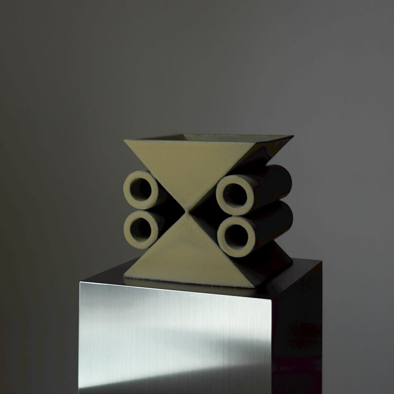 A geometric sculpture with triangular and cylindrical shapes on a metallic pedestal.