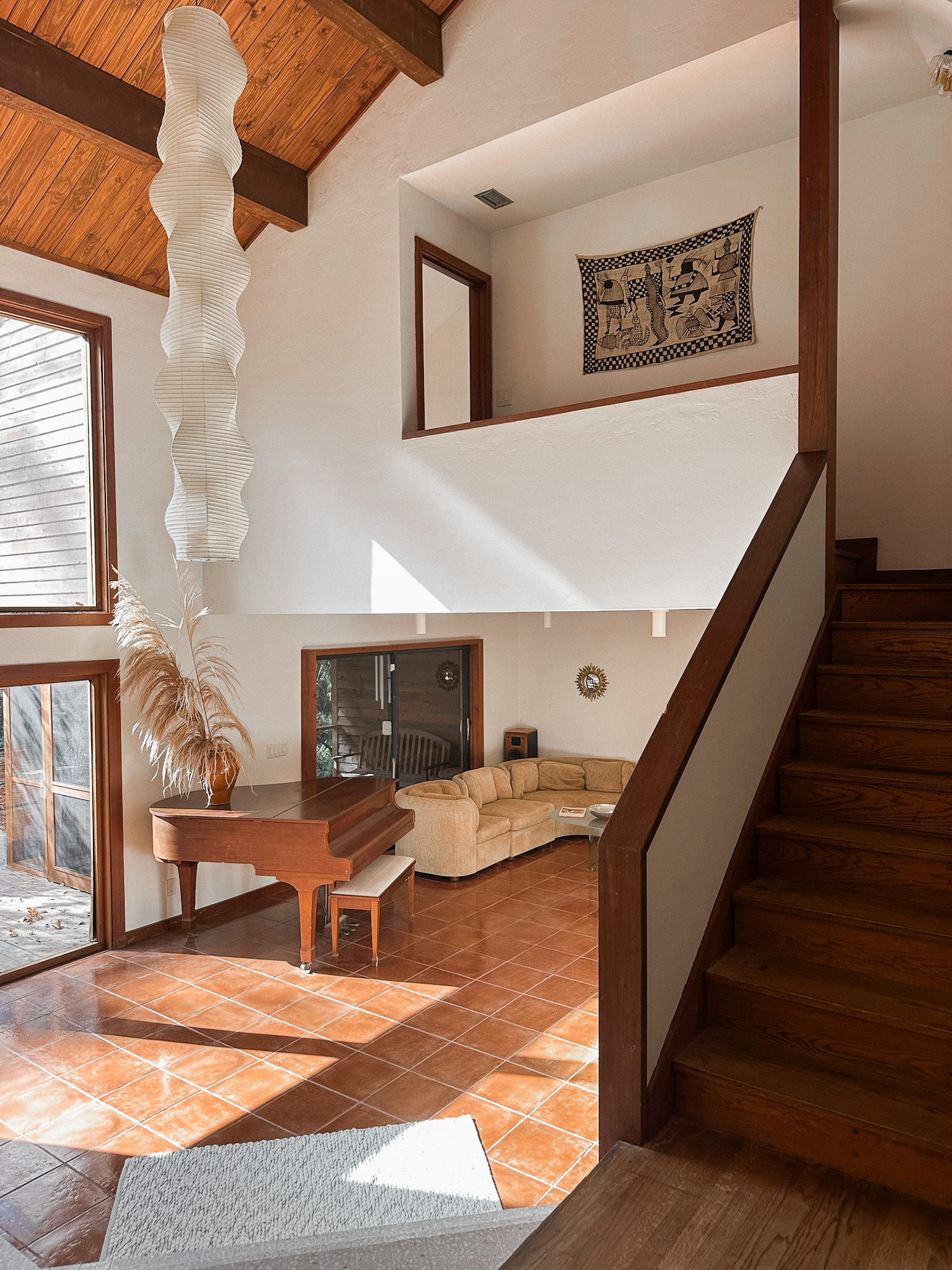 Sunken living room with a reupholstered sectional sofa, baby grand piano, and a large Noguchi paper lantern hanging from the wood ceiling.